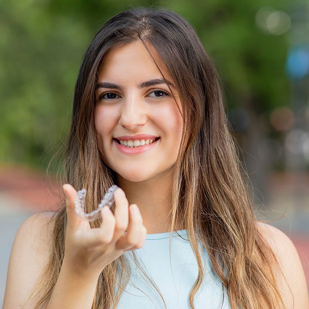 Beautiful smiling woman is holding an invisalign bracer