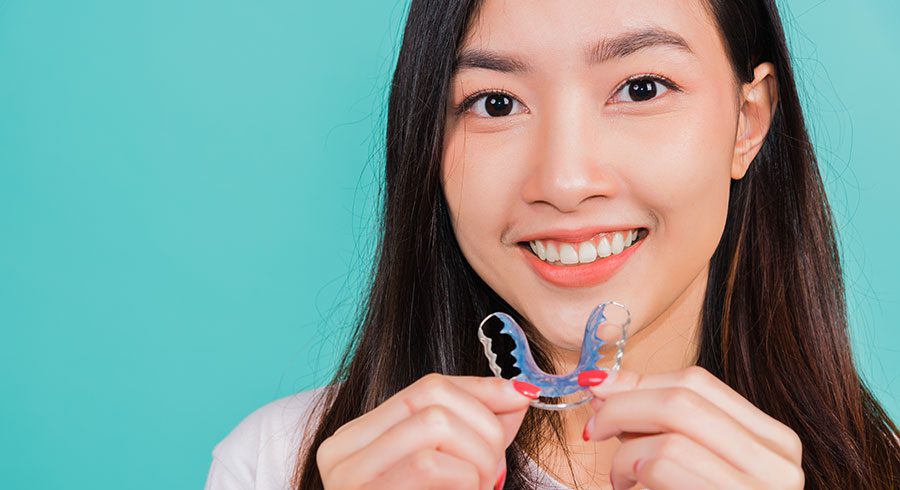 young beautiful woman smiling holding silicone orthodontic retainers for teeth