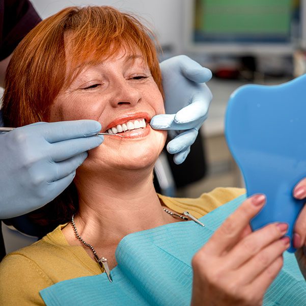 Smiling senior woman with new dental implants sitting in the dental office and looking at the mirror